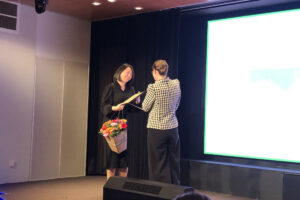 Afbeelding van juryvoorzitter Trude Dijkstra die de oorkonde overhandigt aan winnaar Yun Xie.